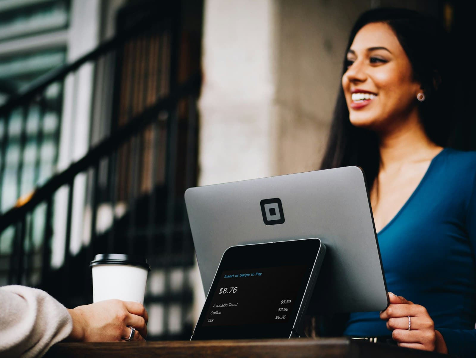 Counter worker holding a Square card reader while a customer pays at pickup