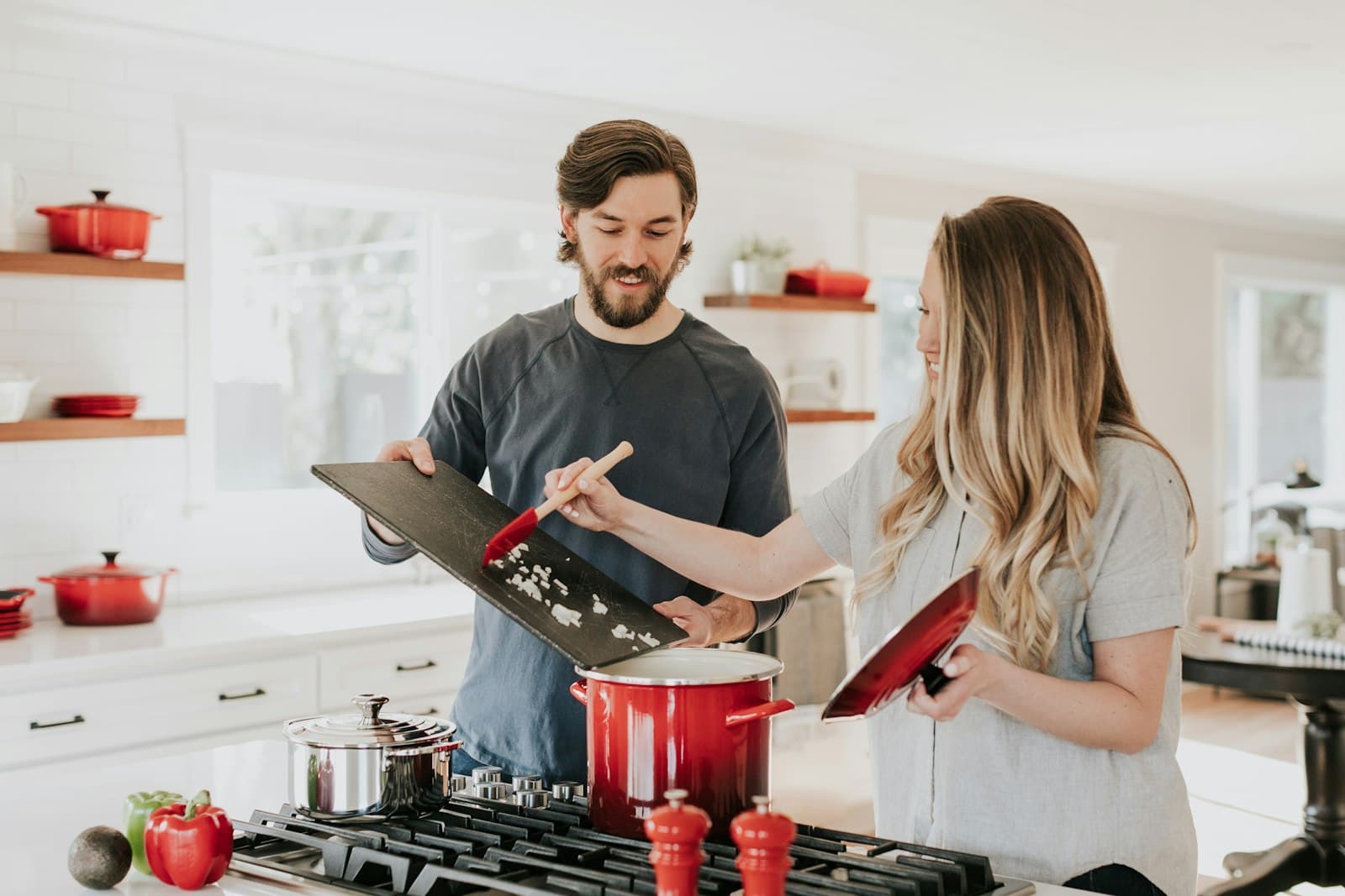 Two people cooking at a home stove, sliding chopped onions from a board into a red pot