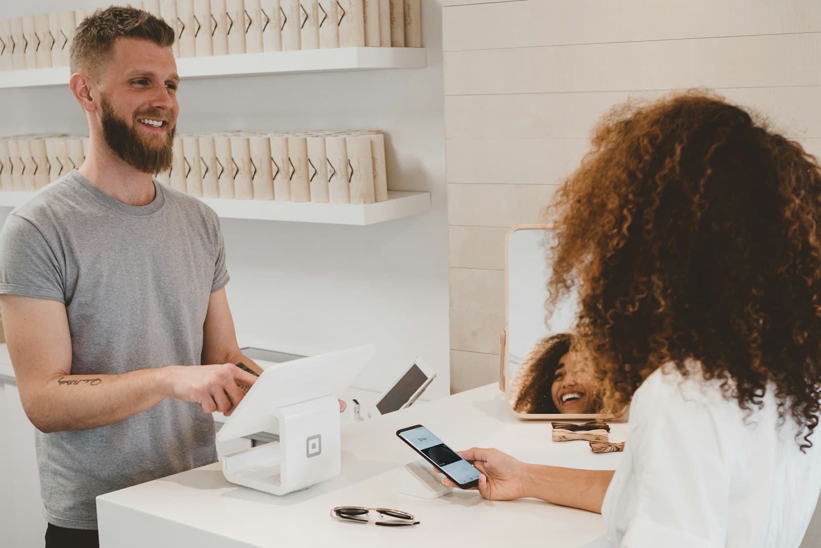 Cashier smiling at a white counter while a customer holds her phone over the card reader