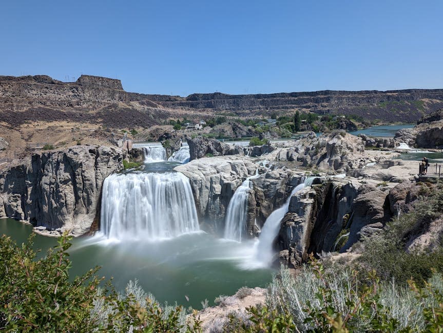Snake River Falls in downtown Idaho Falls, Idaho, with the LDS Idaho Falls Temple rising on the west bank and the Greenbelt path tracing the riverside.