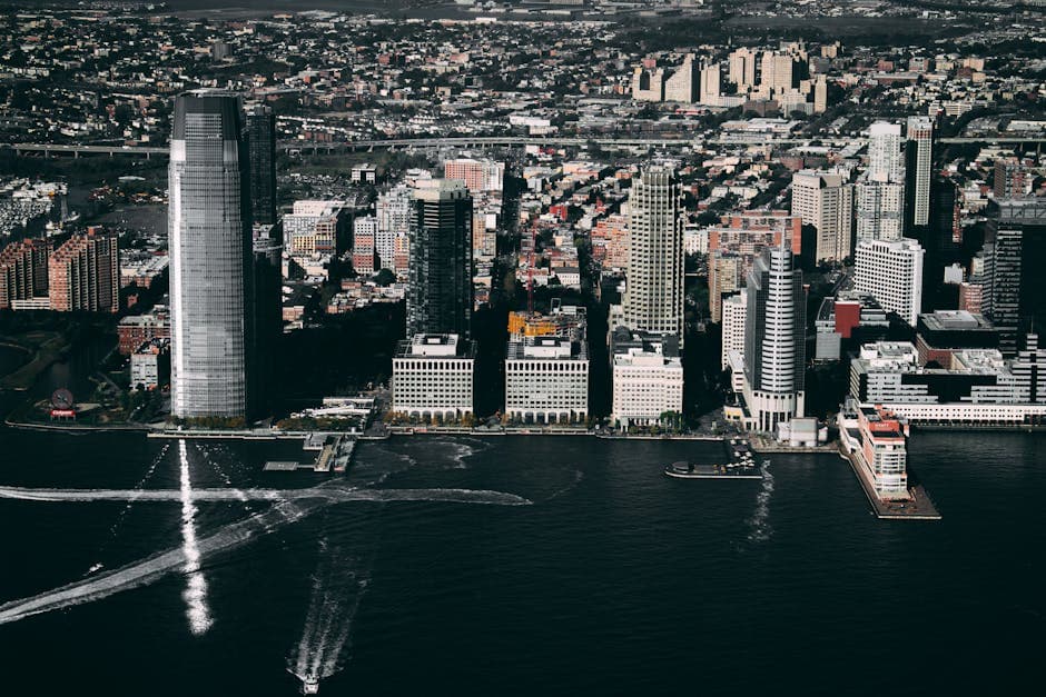The Jersey City skyline across the Hudson River, the Goldman Sachs Tower and the Colgate Clock visible from the waterfront.