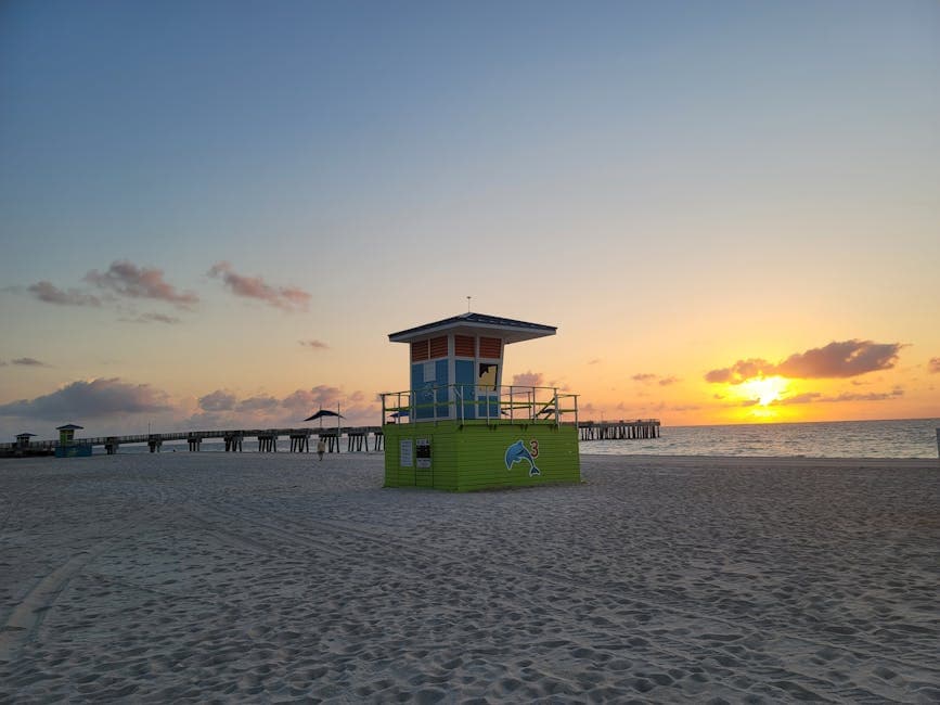Pompano Beach pier at sunrise with the Hillsboro Lighthouse on the horizon and the Atlantic Ocean breaking against the pylons