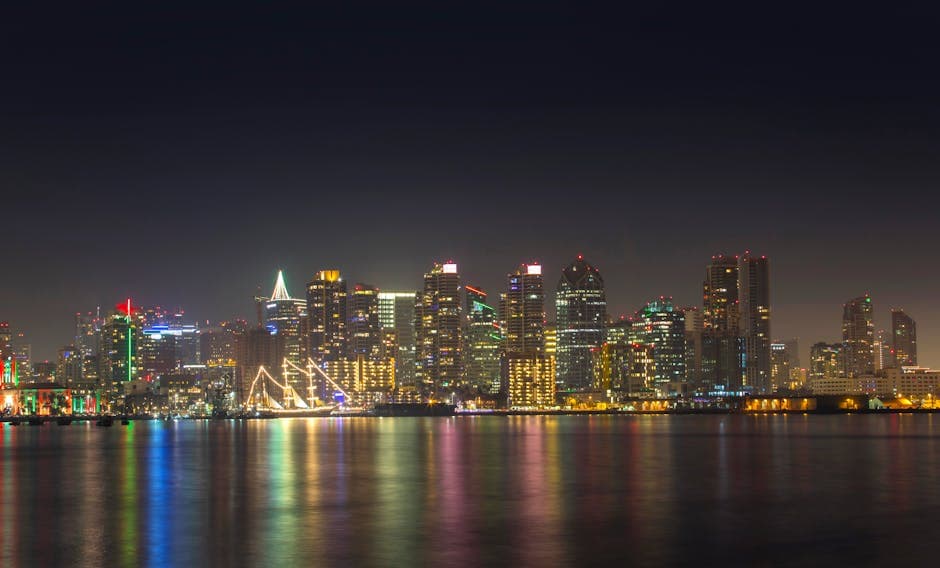 San Diego coastline with Coronado Bridge, the Tijuana skyline visible in the haze, and the downtown waterfront at golden hour