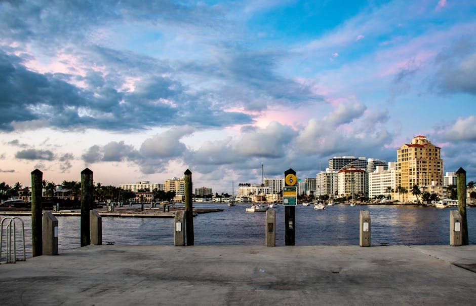 A West Palm Beach scene at dusk with palms, the Intracoastal, and the silhouettes of Palm Beach Island across the water.